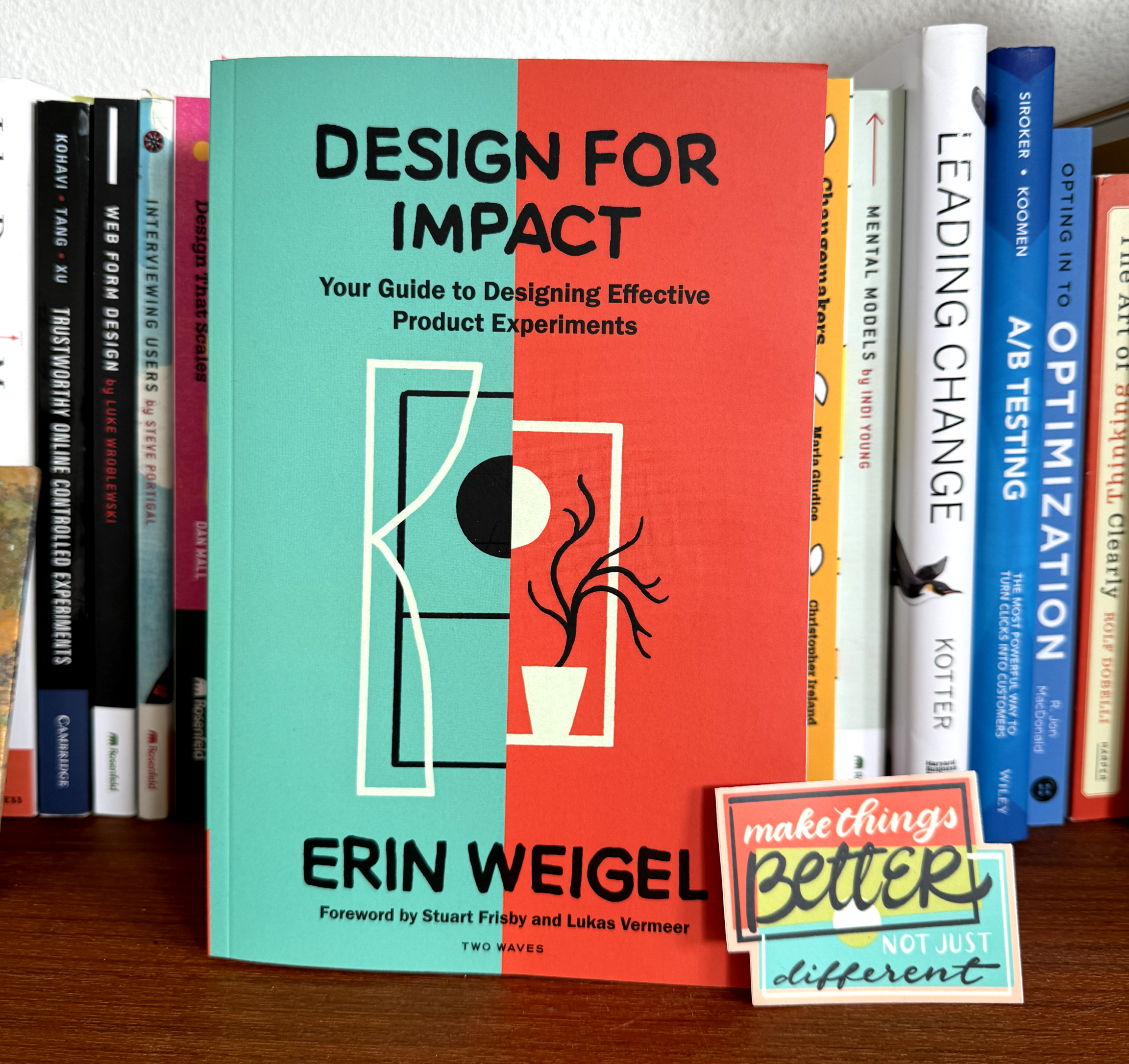 Design for Impact: Your Guide to Designing Effective Product Experiments book by Erin Weigel on a bookshelf. Propped up against the book is a die cut sticker that says, "Make things better—not just different"